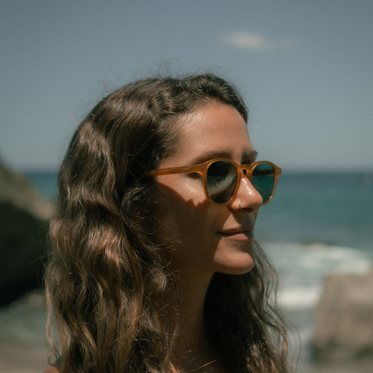 Woman wearing sunglasses with a beach and ocean in the background